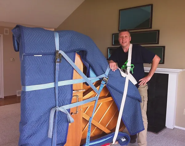 Man poses next to furniture wrapped in blue blankets and straps indoors
